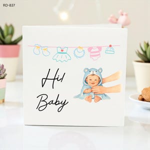 Könnte beinhalten: Weiße Grußkarte mit dem Text "Hi! Baby" in schwarzer Schrift. Die Karte zeigt ein Baby in einem blauen Handtuch mit Bärenmotiv und eine Wäscheleine mit Illustrationen von Babykleidung.