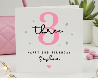 May include: A square white birthday card featuring a large pink number three, the word three in black script, and small grey stars. The text reads HAPPY 3RD BIRTHDAY followed by the name Sophia in black script and a small pink heart below.