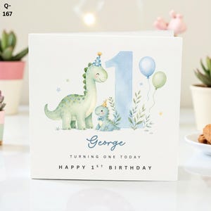 May include: A square birthday card featuring a watercolour illustration of two dinosaurs, a number one, and balloons. The card reads "George", "Turning One Today", and "Happy 1st Birthday". The dinosaurs are wearing party hats.