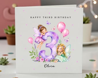 May include: A white square birthday greeting card featuring the text HAPPY THIRD BIRTHDAY and the name Olivia. The design includes a large purple number three, two illustrated fairies with wings, pink balloons, butterflies, and flowers.