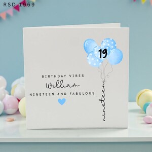 May include: A white square birthday greeting card featuring a cluster of light blue balloons with the number 19. The text reads BIRTHDAY VIBES, William, NINETEEN AND FABULOUS, and the word nineteen written vertically along the balloon strings with a blue heart.