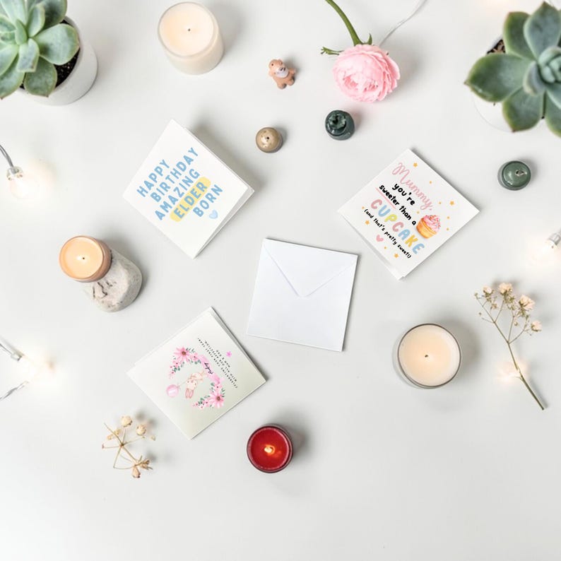 Puede incluir: Tarjetas de felicitaci&oacute;n con texto, velas y flores dispuestas sobre una superficie blanca. Una tarjeta dice "Happy Birthday Amazing Elder Born". Otra dice "Mummy you're sweeter than a cupcake". Tambi&eacute;n hay un sobre blanco.
