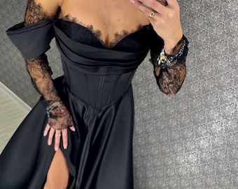 May include: A black off-the-shoulder dress with a corset bodice and a high slit. The dress features lace sleeves and trim along the neckline. The dress is made of a shiny, flowing fabric.