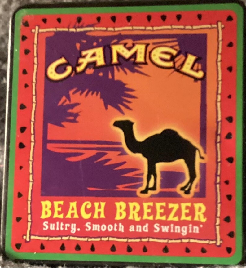 May include: A rectangular graphic with a red border and a green outline. The graphic features the word "CAMEL" in yellow, a black camel silhouette, and the text "BEACH BREEZER" with the tagline "Sultry. Smooth and Swingin'". The background has purple, orange, and blue hues.