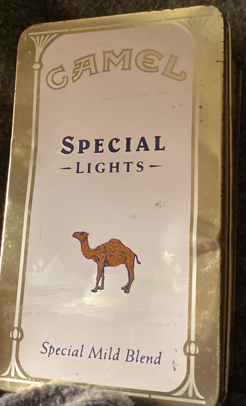May include: Vintage Camel Special Lights cigarette tin. The tin has a gold border and a white background with the Camel logo at the top. The text "SPECIAL - LIGHTS -" is in the center, with a camel illustration below. "Special Mild Blend" is at the bottom.
