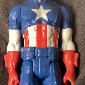 May include: A Captain America action figure. The figure is predominantly blue, red, and white, with a large white star on the chest. The head is blue with a white "A" on the forehead. The figure has red gloves and boots.