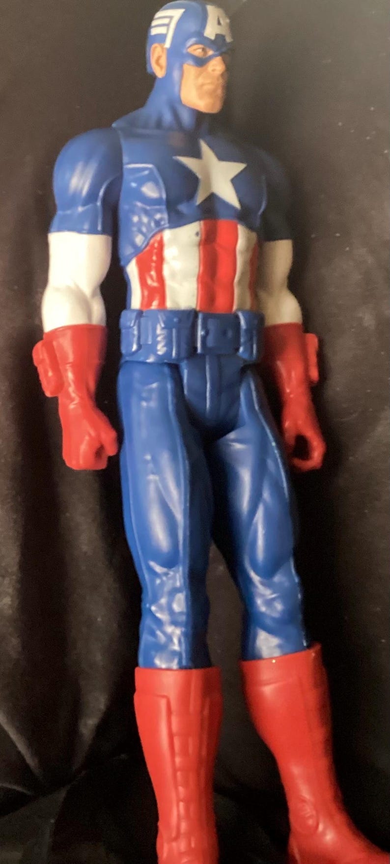 May include: A Captain America action figure. The figure is wearing a blue and white helmet, a blue suit with a white star, and a red, white, and blue torso. The figure has red gloves and boots.