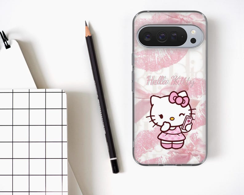 May include: A clear phone case featuring a pink Hello Kitty design. The case has a pink bow and dress, holding a phone. The background has pink lips and the words "Hello Kitty". A black pencil and a notepad are on the white surface.