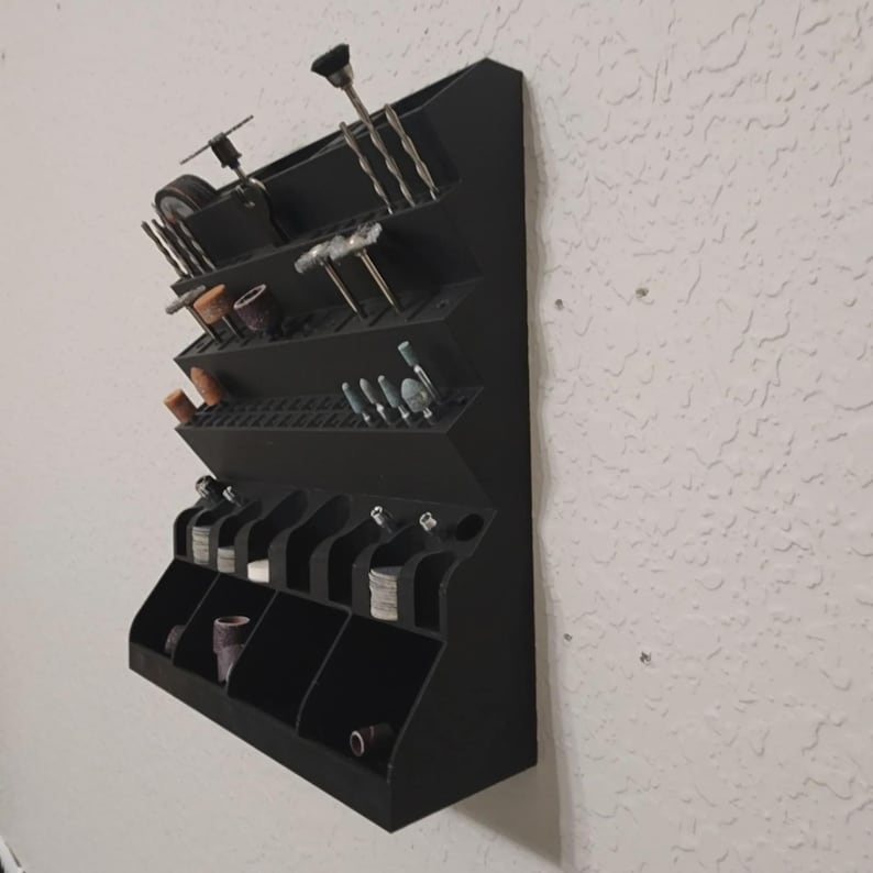 May include: A black wall-mounted organizer for small tools, featuring multiple angled shelves and compartments. Various tools, including drill bits and grinding accessories, are neatly arranged within the organizer, providing a structured storage solution.