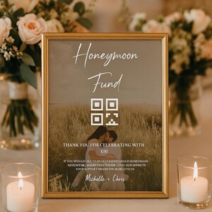 Könnte beinhalten: Ein gerahmtes Schild mit den Worten "Honeymoon Fund" in eleganter Schrift. Darunter ein QR-Code und ein Foto eines sich küssenden Paares. Der Text lautet "Danke, dass Sie mit uns feiern!" und "Michelle + Chris."