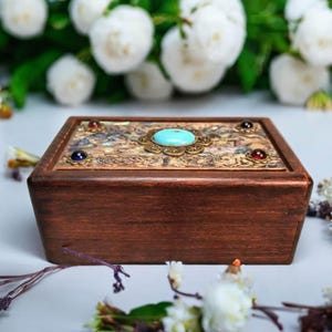 May include: A wooden box with a decorative top featuring a turquoise stone surrounded by a brass design. The box is made of dark wood and has a natural wood grain.