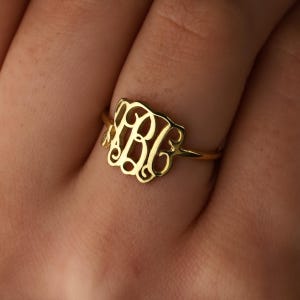 May include: A gold-toned ring with a monogram design featuring the letters "BJE".