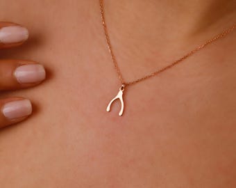 May include: A delicate rose gold necklace featuring a wishbone pendant. The pendant is a simple, curved design, suspended from a fine chain. The necklace is shown against a skin tone background.