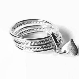 May include: A stack of silver rings with a textured design and a small heart charm. The rings are made of a shiny metal and are stacked together. The heart charm is attached to the rings with a small loop.