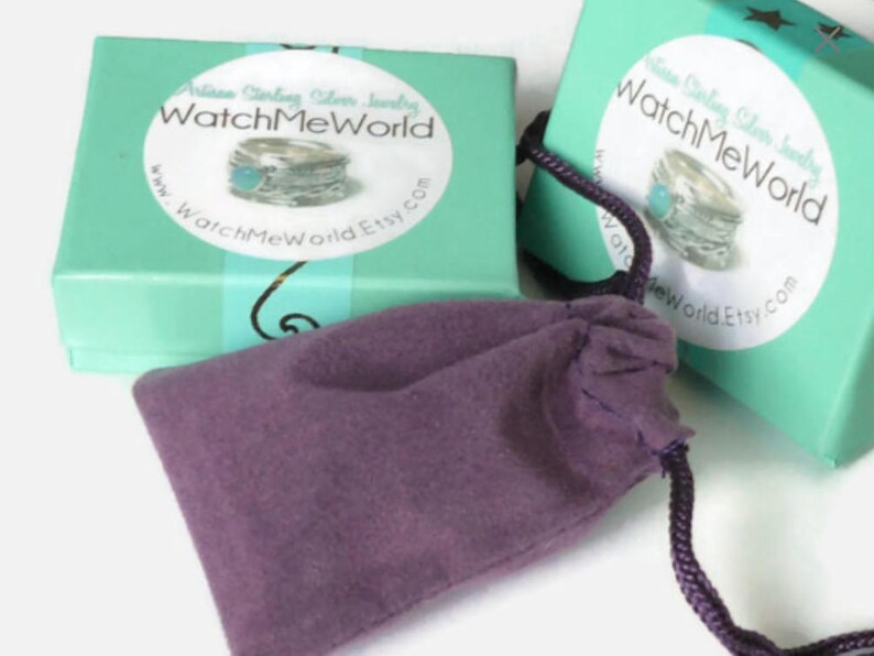 Pode incluir: Duas caixas turquesa com o texto "WatchMeWorld" e uma imagem de anel na frente. Uma bolsa roxa com cord&atilde;o est&aacute; em frente &agrave;s caixas. As caixas s&atilde;o de cor verde-azulado claro.