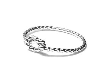May include: A silver-colored ring with a knot design. The ring has a twisted rope-like band that forms a knot at the center. The ring is set against a white background.