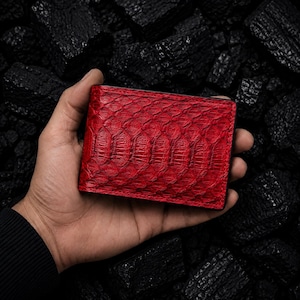 May include: A rectangular bifold wallet featuring a vibrant red snakeskin texture with a distinct scale pattern. The wallet has clean, straight edges and a slim profile, showcasing a bold, saturated crimson color throughout the exterior surface.