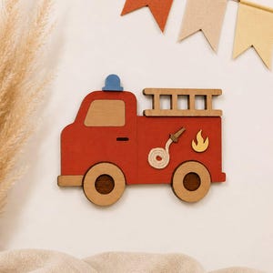 May include: A wooden fire engine cutout featuring a red body, a blue light on top, a tan ladder, and two wheels. The side of the engine displays a coiled white rope hose and a yellow flame graphic. The design is flat and crafted from layered wood pieces.