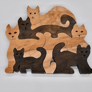 Könnte beinhalten: Ein Holzpuzzle mit sieben Katzen, jede mit einer einzigartigen Form und einem einzigartigen Design. Die Katzen sind aus hellem und dunklem Holz gefertigt, was ein kontrastierendes Muster erzeugt. Das Puzzle ist eine lustige und herausfordernde Aktivität für Menschen jeden Alters.