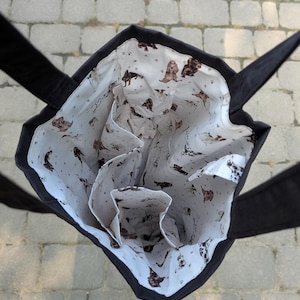 May include: A black tote bag with a white interior lining featuring a repeating pattern of brown and white spaniel dogs and small paw prints. The bag has two black fabric handles and internal pockets visible from an overhead perspective.
