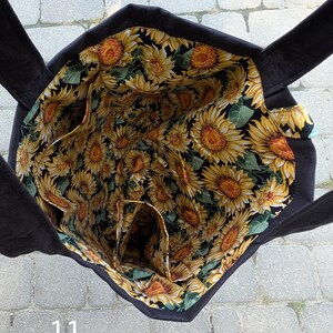 May include: A black tote bag with a sunflower print lining featuring yellow petals, brown centers, and green leaves on a black background. The interior includes multiple pockets and two black fabric handles extending from the top edges.