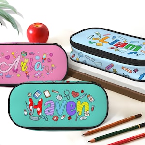 May include: Three personalized pencil cases in pink, blue, and teal, each with a black zipper. The pink case says "Aria" with decorative elements. The blue case says "Liam". The teal case says "Haven" with medical-themed illustrations. Pencils and an apple are also present.