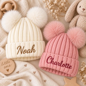 Puede incluir: Dos gorros de punto acanalado con dos pompones. Un gorro es de color crema con el nombre Noah bordado en marrón. El otro gorro es de color rosa empolvado con el nombre Charlotte bordado en rosa oscuro. Ambos tienen un borde doblado.