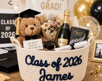 May include: A cream-coloured graduation gift basket with navy blue text reading "Class of 2026 James". The basket contains a teddy bear in a graduation cap, a bottle of Freixenet, flowers, chocolates, and a congratulatory scroll.