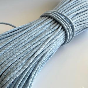 May include: A bundle of light blue rope, tightly wound and secured with a matching cord. The rope has a textured, woven appearance, and the color is a soft, pastel blue. The product is suitable for various crafting and decorative purposes.