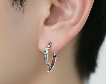 May include: A close-up of a person's ear with a silver hoop earring. The earring has a unique design, with a curved shape and a textured surface. The earring is a stylish accessory.