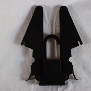 May include: Black plastic hanger with a hook and two wings that fold down. The hanger is designed to hold a garment in place.