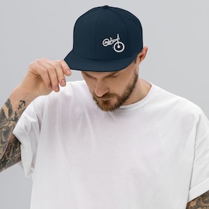 Puede incluir: Una gorra de béisbol azul marino con un diseño de bicicleta de montaña bordado en blanco.