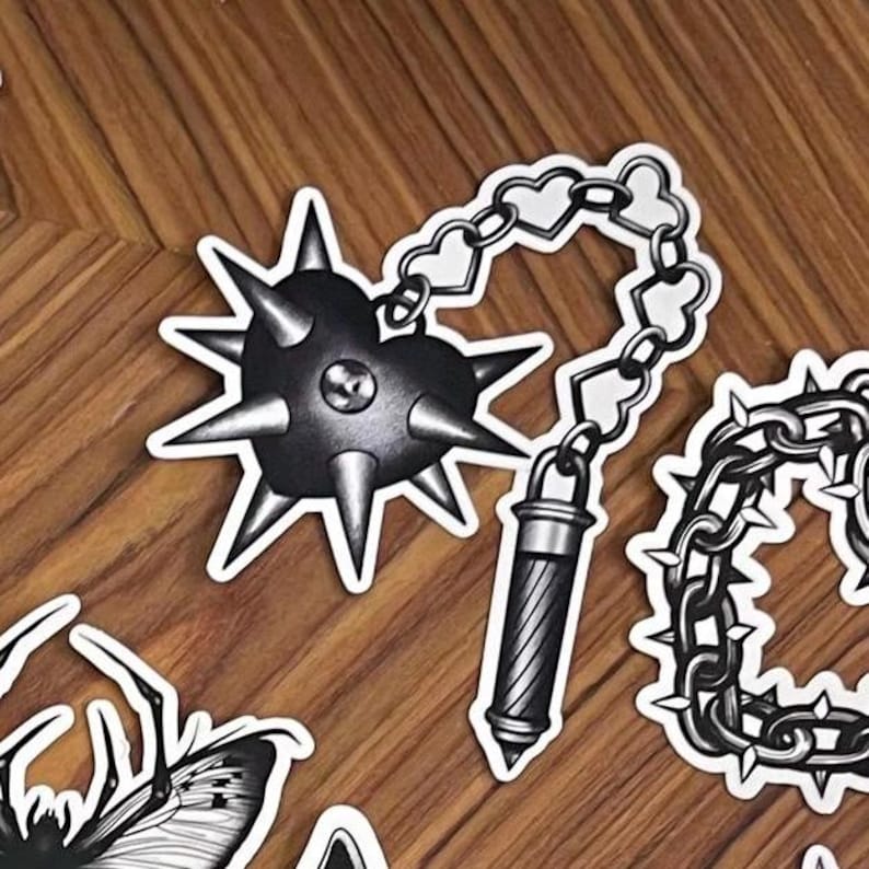 May include: Black and white sticker of a spiked mace connected by a chain of hearts to a cylindrical object. The mace has sharp spikes and a heart-shaped center. The chain links are heart-shaped.