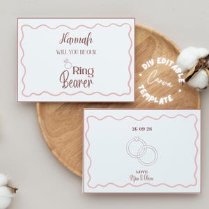 Op de afbeelding: Twee witte uitnodigingskaarten met een roze geschulpte rand. Eén kaart leest "Hannah, Will You Be Our Ring Bearer" in een scriptlettertype. De andere kaart heeft de datum "26 09 28" en het woord "LOVE" met namen.
