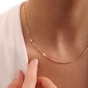 Puede incluir: Un delicado collar de cadena de oro con un pequeño dije de cruz y una sola piedra preciosa transparente.