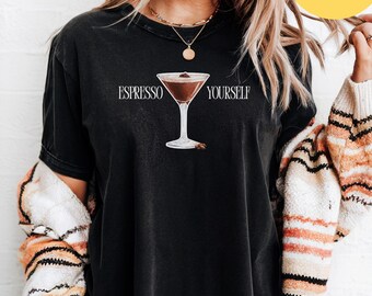 May include: Black t-shirt with the phrase "ESPRESSO YOURSELF" printed above a graphic of a martini glass filled with a coffee-colored drink. The shirt has a relaxed fit and short sleeves.