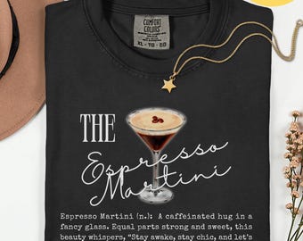 May include: Black t-shirt with a graphic of an espresso martini in a fancy glass. The text reads "THE Espresso Martini" and includes a definition. A gold star pendant necklace is draped on the shirt.