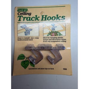 May include: Package of clear plastic ceiling track hooks. The packaging is tan with green text that reads "hold-all Ceiling Track Hooks". The hooks are designed for hanging plants and decorative items. The package also includes installation tips.