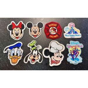 Puede incluir: Una colección de parches bordados de personajes de Disney, incluyendo Mickey Mouse, Minnie Mouse, Donald Duck, Goofy y Mickey como chef. Otros parches presentan el logotipo de Walt Disney World y un emblema de Mickey's Fire Dept. Los parches son coloridos y detallados.