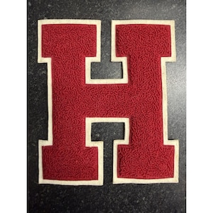 May include: A varsity-style letter H patch featuring a textured, deep red chenille center with a thick, smooth off-white felt border. The block-style letter has a classic collegiate appearance with a raised, fuzzy surface and clean, defined edges.