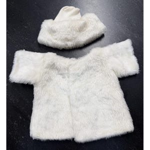 May include: A white faux fur short-sleeved top and a matching white faux fur hat. The top features a straight hemline and a wide neckline, while the hat has a rounded crown and a thick, textured brim, both made of soft, long-pile white material.