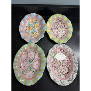 May include: Four oval ceramic bowls with scalloped edges, each featuring hand-painted floral designs in pastel colors. The bowls display varied patterns of yellow and pink flowers, surrounded by striped or dotted borders in blue, green, and pink.