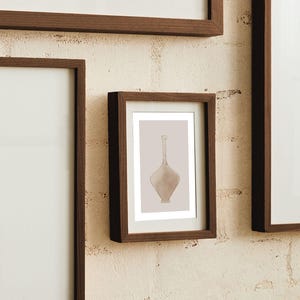 May include: A framed wall art print featuring a centered illustration of a light beige glass bottle with a long, slender neck and a wide, tapered body, set against a solid light beige background within a dark brown wooden frame.