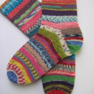 May include: A pair of hand-knitted socks with a vibrant striped pattern in shades of pink, blue, green, and yellow. The socks feature a ribbed cuff and heel, and are made from soft yarn.