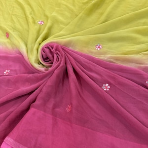 May include: A draped fabric in shades of yellow and pink, with a gradient effect. The fabric is adorned with small, embroidered flower details. The material appears lightweight and flowing, suggesting a scarf or shawl.