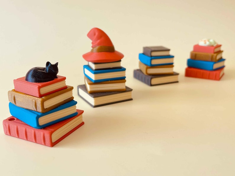 May include: A collection of miniature book stacks in various colors, including red, blue, and brown. One stack features a black cat figurine, while another has a red witch hat. The theme suggests a fantasy or literary concept.
