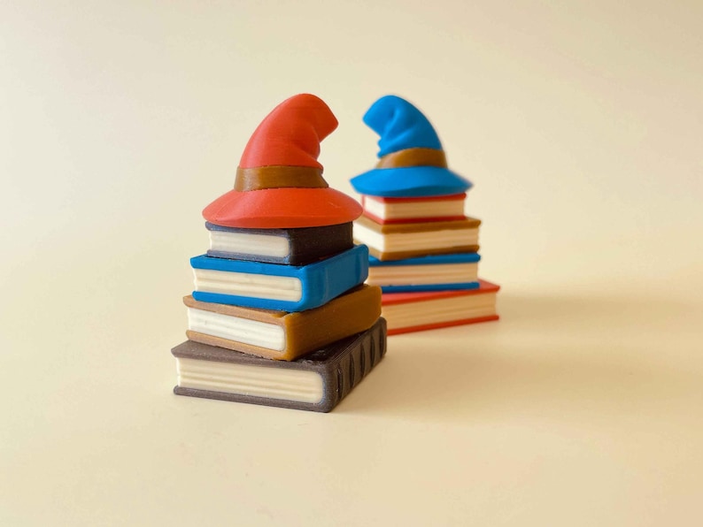 May include: Two stacks of books topped with wizard hats. One stack has a red hat, the other a blue hat. The books are various colors, including brown, blue, and black, with white pages. The hats have brown bands.