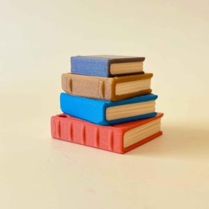 May include: A stack of four miniature books in red, blue, tan, and dark blue. The books are stacked on top of each other, with the red book at the bottom and the dark blue book at the top. The pages are a light tan color.