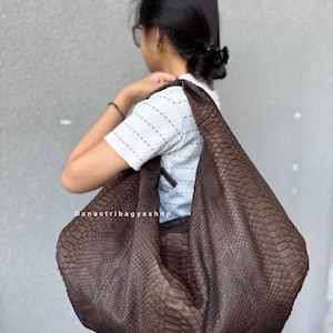 Può includere: Una grande borsa a tracolla in pelle marrone con un motivo a pelle di serpente. La borsa è indossata sulla spalla. Il testo "Danastribagyashop" è visibile sulla borsa.