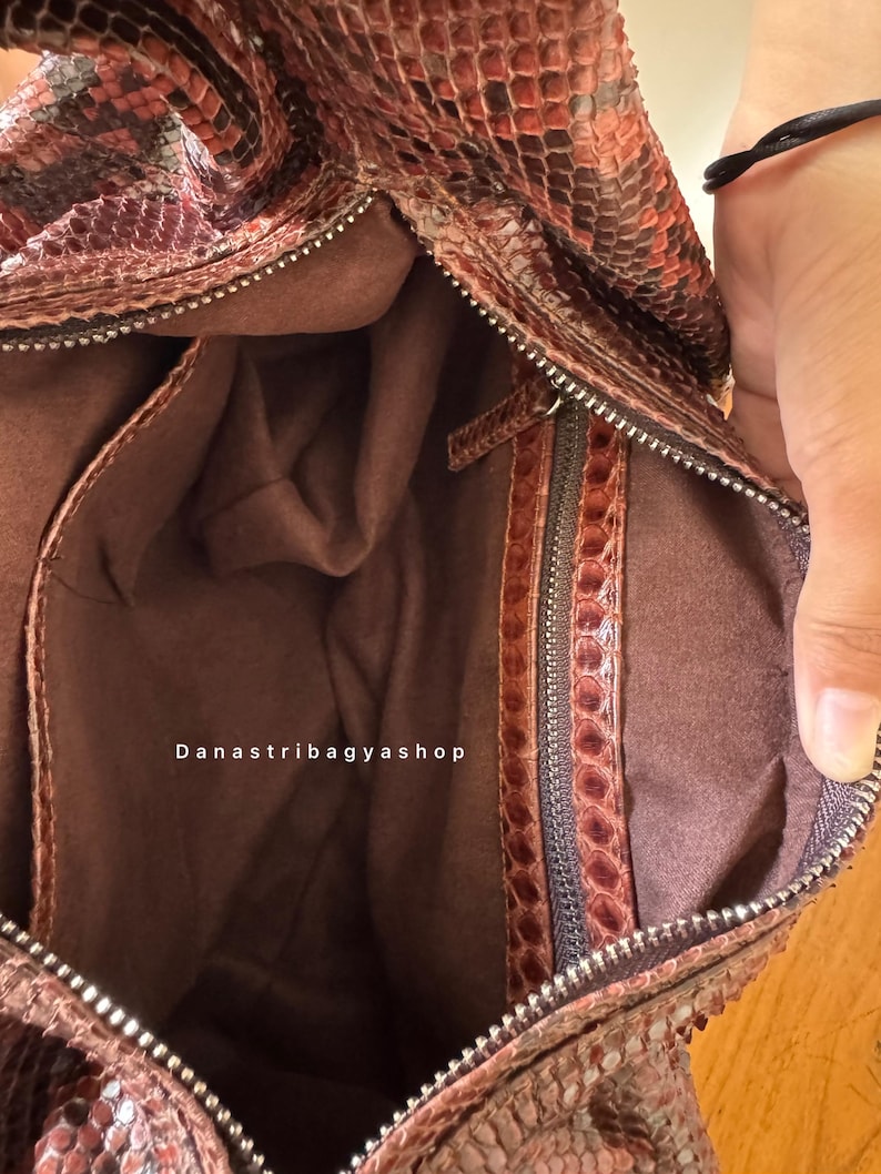Peut inclure: Vue ouverte d'un sac &agrave; main marron et rouge &agrave; motif peau de serpent. L'int&eacute;rieur est de couleur marron uni, avec une fermeture &eacute;clair et une petite poche zipp&eacute;e. Le texte "Danastribagyashop" est visible.